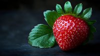 Fresh ripe strawberry with green leaves on dark background, dramatic lighting creates contrast between bright red fruit and moody setting.