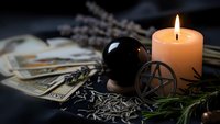 Mystical fortune telling setup with tarot cards, crystal ball, pentagram symbol and burning candle creating atmospheric divination scene for spiritual practices.