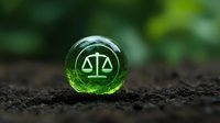 Green glass marble with scales of justice symbol placed on soil, representing environmental law and ecological balance.