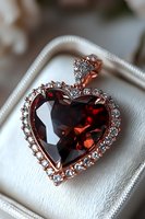 Elegant heart-shaped garnet pendant with diamond halo in rose gold setting, displayed on white jewelry box cushion, capturing romantic luxury and sparkle.
