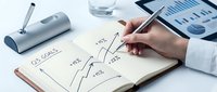 Business professional drawing upward trending graph showing growth from 10% to 25% in notebook with charts and water glass on desk for financial planning.