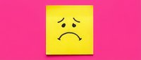 Yellow sticky note with sad face drawn in black ink on bright pink background expressing disappointment and negative emotions for office communication.