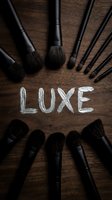Makeup brushes with black handles arranged in circle around word written in chalk on wooden surface, cosmetics and beauty tools for professional application.