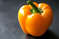 Fresh orange bell pepper with green stem on dark slate surface for healthy cooking and nutrition concepts.