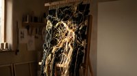 Handwoven macrame wall hanging with natural fiber tassels and wooden dowel rod displayed on easel in modern interior space for bohemian home decor.
