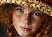Young redhead woman with freckles wearing straw hat smiling at camera in warm sunlight. Natural beauty portrait for lifestyle and summer concepts.