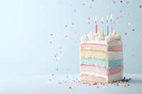 Colorful pastel rainbow layer cake slice with white frosting and lit birthday candles on light background with confetti sprinkles, celebration dessert.
