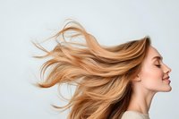 Young Caucasian woman with flowing blonde hair against light background, eyes closed with natural smile, showing hair movement and healthy shine.