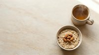 Overhead view of oatmeal bowl with almonds and coffee cup on neutral beige linen surface, ideal for breakfast, nutrition, and wellness content.