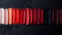 Colorful lipstick swatches arranged in gradient from pink to red to dark shades on black background for cosmetic beauty makeup product testing.
