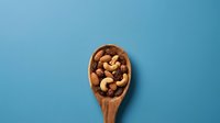 Mixed nuts and dried fruits in wooden spoon on blue background. Healthy snacking, organic food ingredients for cooking and baking recipes.