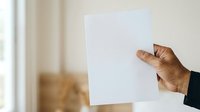 Mature male hand holding blank white paper sheet against neutral background, suitable for advertising, marketing mockups, presentations, and business communications.