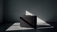 Sleek black hard-shell briefcase on a dark floor with dramatic sunlight shadows, conveying luxury, travel, and business elegance.