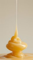 Thick golden honey dripping and forming a swirling shape against neutral background, capturing liquid motion and viscosity in soft natural lighting.