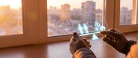 Hands holding transparent glass panel with glowing work-life balance scale hologram, city skyline at sunset in background, business concept.