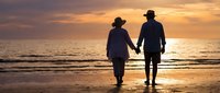 Senior couple walking hand in hand on beach at sunset, romantic silhouettes against golden sky and ocean waves, peaceful retirement lifestyle moment.