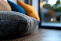 Cozy home interior with soft gray linen cushion in foreground, yellow and blue pillows blurred in background, window view creating peaceful domestic atmosphere.