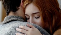 Young woman with red hair embracing partner wearing gray sweater, intimate emotional moment showing tenderness, comfort and support in relationship.