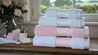 Stack of soft cotton towels in white and pink colors neatly folded on wooden surface near bathroom window with flowers creating spa-like atmosphere.