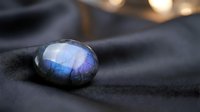 Blue labradorite gemstone with natural flash on dark fabric surface, crystal healing stone for jewelry making and spiritual practices.
