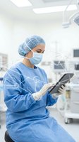 Female surgeon in blue scrubs using tablet in operating room with glowing digital network overlay for healthcare technology.