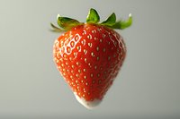 Fresh ripe strawberry with green leaves isolated on light background, showcasing vibrant red color and textured surface with visible seeds.