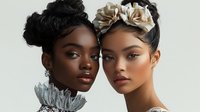 Two young women with floral headpieces and dramatic ruffled collars pose together against neutral background, showcasing contrasting beauty and fashion styling.