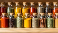 Colorful spices and herbs in glass jars with cork lids arranged on wooden shelf for cooking and seasoning culinary ingredients storage organization.