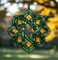 Celtic knot suncatcher in emerald green glass with amber crystal accents creates magical light effects against blurred natural background. For spiritual decor.