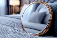 Round vintage mirror with ornate golden frame on gray textile surface, soft bedroom interior with blurred lamp in background, selective focus on decorative border.