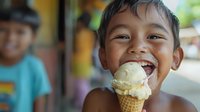 Happy Asian boy enjoying vanilla ice cream cone with joyful expression, summer childhood treat outdoors.