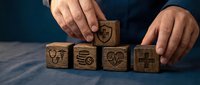Caucasian male hands arranging wooden blocks with healthcare icons including heartbeat, medical cross, and stethoscope symbols on blue surface for health insurance and wellness concept.