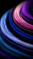 Colorful braided cables in vibrant blue, pink and purple hues create curved lines against black background, macro photography showing detailed texture pattern.
