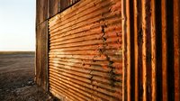 Weathered corrugated metal fence with rust and oxidation standing in barren landscape at golden hour, suitable for industrial, rural, and architectural design projects.
