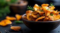 Fresh golden chanterelle mushrooms with rosemary herbs in rustic wooden bowl on dark slate surface. Organic forest fungi ingredients for gourmet cooking and culinary recipes.