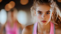 Young athletic woman in pink tank top with determined expression against blurred bokeh background. Focused gaze and natural makeup for fitness and wellness concepts.