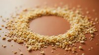 Scattered golden granules form a circular frame on warm neutral background, creating textured border pattern for design projects and creative compositions.