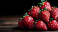 Fresh ripe strawberries with green leaves on dark wooden background, macro shot with selective focus and copy space for food photography.