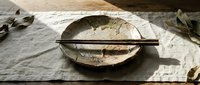 Empty ceramic bowl with chopsticks on linen fabric, rustic Asian tableware setup for dining, food styling, and culinary design projects.