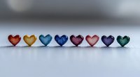 Colorful glass hearts arranged in rainbow sequence on light surface, creating romantic minimalist composition for valentines and love concepts, soft bokeh background.