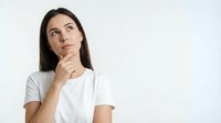 Young brunette woman in white t-shirt looking up thoughtfully with hand on chin, contemplating decision or idea against clean white background.