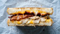 Grilled sandwich with crispy bacon, melted cheese and turkey on toasted bread. Comfort food lunch meal ready to eat on parchment paper background.