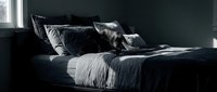 Unmade bed with black and white rumpled bedding and pillows in minimalist bedroom interior with dark walls and natural light.