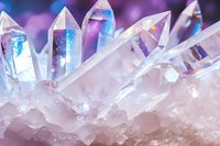 Clear quartz crystal points with blue and purple light reflections on natural mineral cluster formation, macro photography showing transparent crystalline structure.