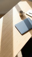 Minimalist workspace with blue laptop on wooden desk, coffee mug and notepad in natural sunlight, ideal for business, productivity and remote work concepts.