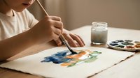 Young artist painting colorful watercolor artwork at wooden table with brush, palette and water jar in natural light for creative hobby projects.