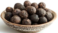 Aromatic black peppercorns in traditional ceramic bowl with ornate pattern on white background, macro food photography showing texture and spice details.
