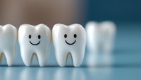 Smiling teeth models in row showing happy healthy dental concept. Close up view of white tooth figurines with drawn smiley faces on blue background.