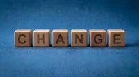 Wooden letter cubes spelling CHANGE on a blue textured fabric background, symbolizing transformation, growth, and new beginnings in business and life.