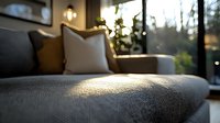 Sunlit modern sofa with textured gray upholstery and decorative pillows in contemporary living room setting. Natural light creates atmospheric bokeh effect through window.